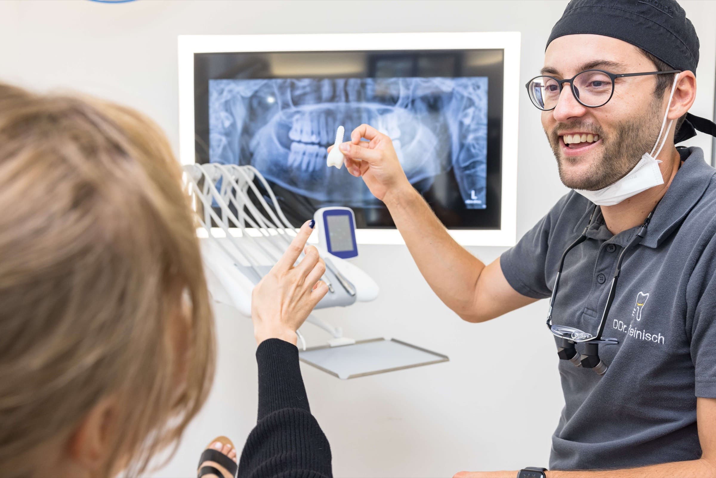 DDr. Reinisch erklärt einer Patientin ein Implantat vor dem Röntgenbild in der Ordination dentalReinisch