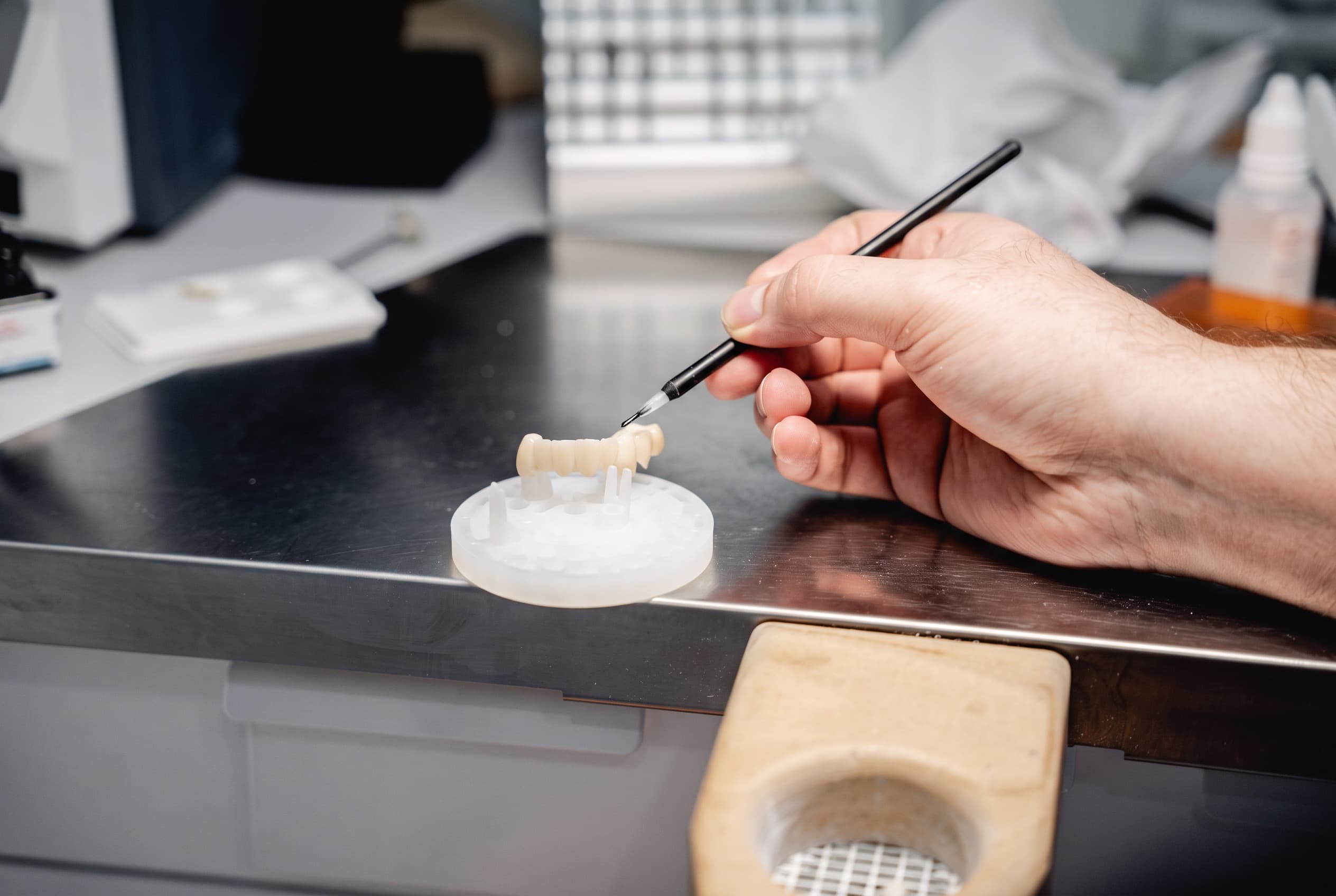 Hand bemalt eine gefräste Zahnbrücke am Arbeitstisch der Zahntechnik bei dentalReinisch